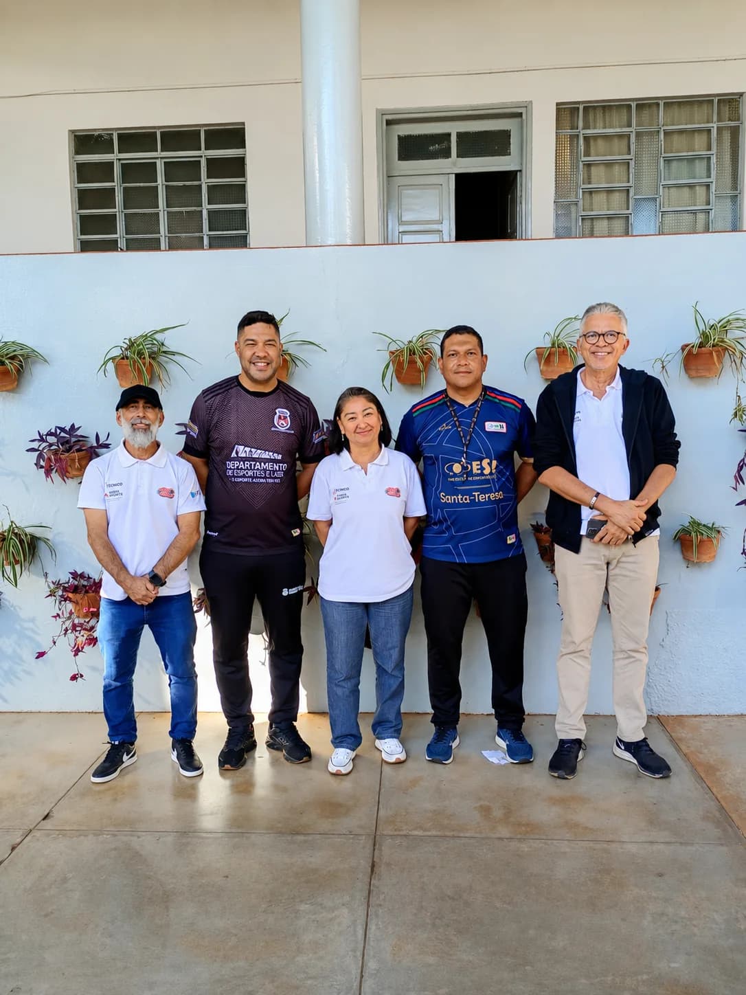 Cinco profissionais reunidos diante de um muro azul-claro com vasos de plantas