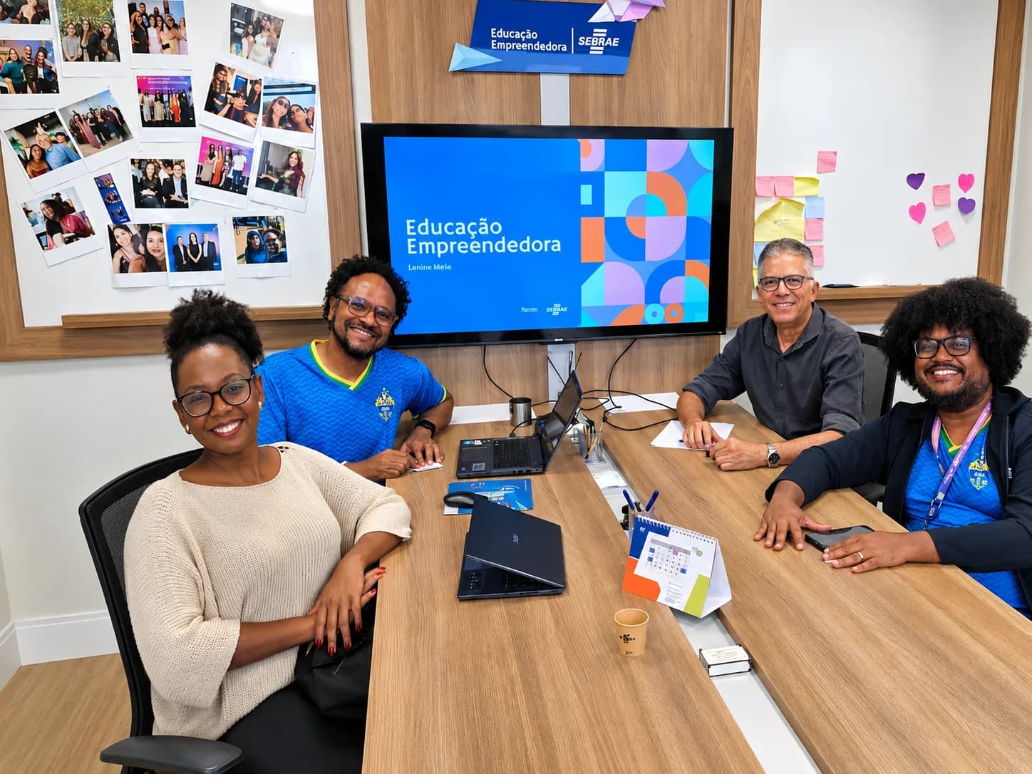 Quatro pessoas reunidas em uma sala de articulação educacional, diante de um painel de apresentação