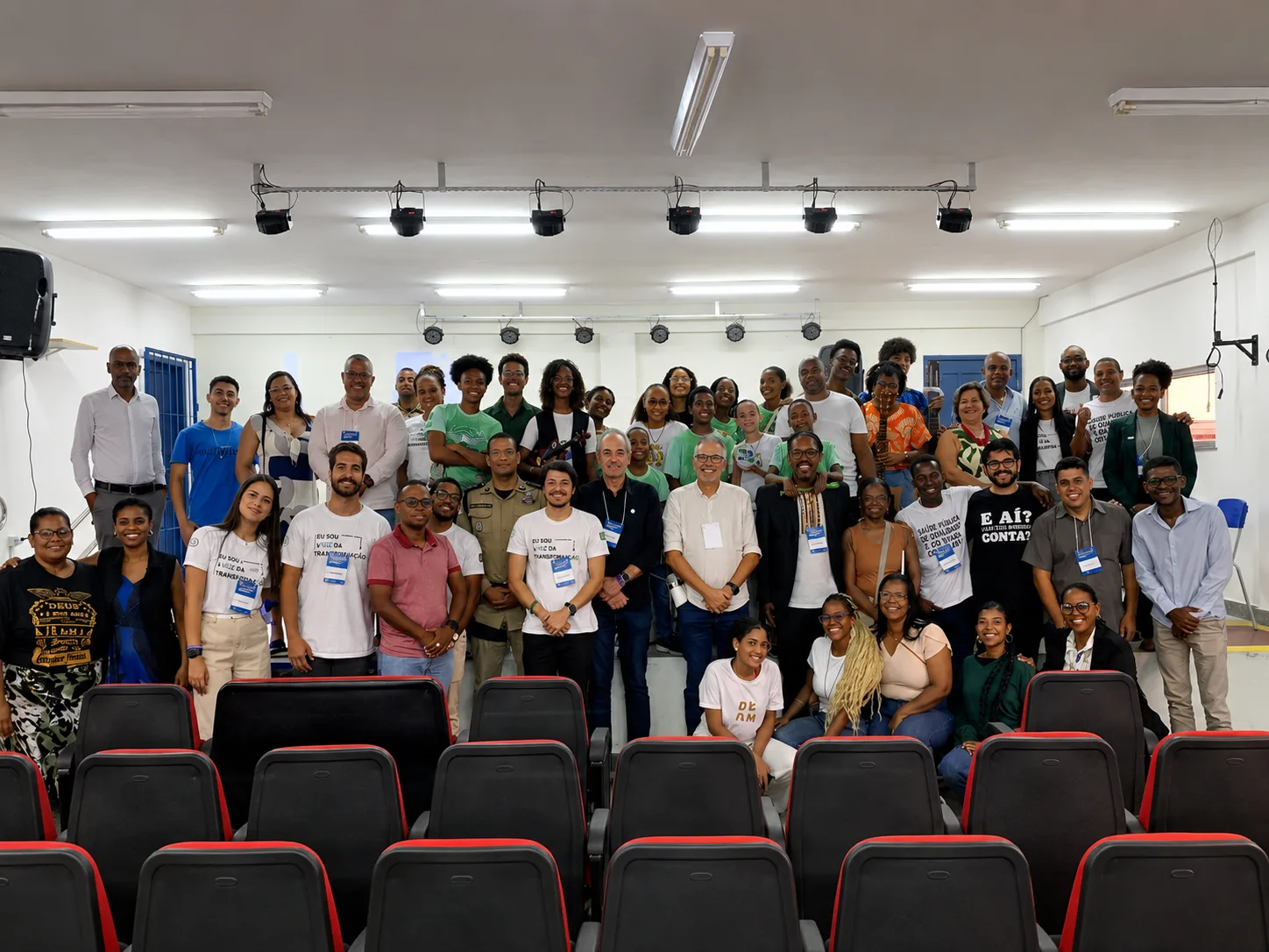 Grupo diverso de participantes reunido na oficina de apresentação do Observatório Educacional, em auditório iluminado
