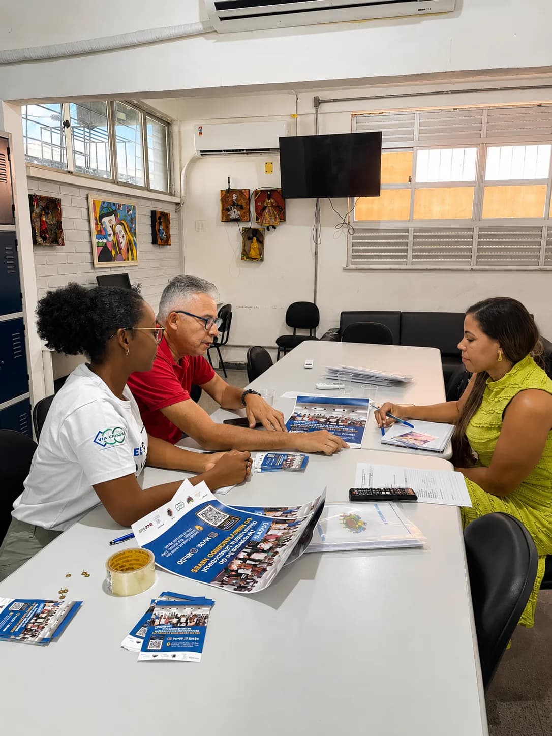 Reunião de trabalho ao redor de uma mesa com materiais impressos e folhetos do Observatório Educacional