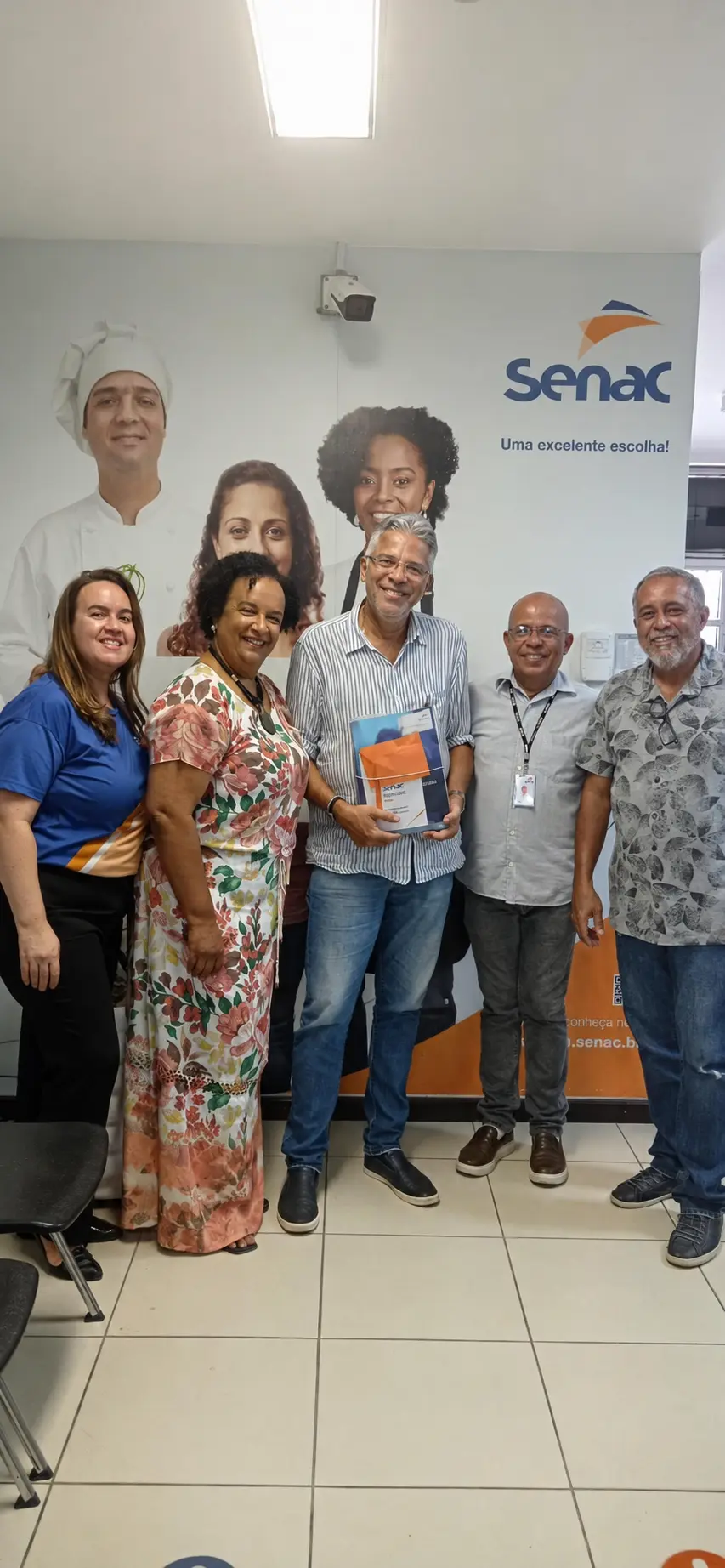 Professor Ney Campello e profissionais reunidos diante da identidade visual do SENAC